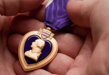A hand holding a Purple Heart medal with a purple ribbon
