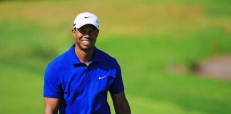 A smiling golfer wearing a blue shirt and white cap on a green golf course