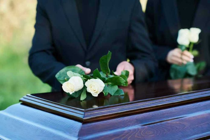 People placing white roses on a casket.