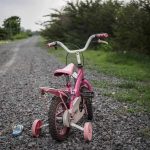 6-Year-Old FOUND Buried in Backyard! Pink childrens bike with training wheels on gravel path.