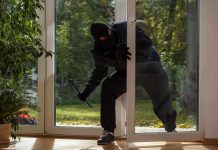 A burglar in dark clothing entering a house through a glass door
