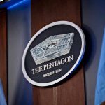 Pentagon Hire J6 Rioter For TOP Position The Pentagon emblem between two flags.