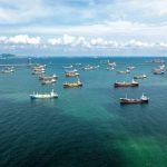 Aerial view of numerous cargo ships anchored in a blue ocean