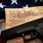 Handgun on U.S. Constitution with American flag backdrop