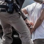 Illegal Migrant ASSAULTS Cop – Grabs Gun police officer handcuffing a person beside a vehicle