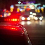 Here’s Why Cops Touch the Back of Your Car Police car with flashing red lights on a city street at night