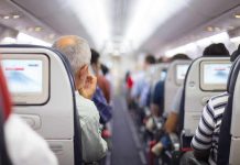 Airplane cabin aisle with passengers seated and seatback screens