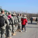 Soldiers in uniform line up outdoors with gear
