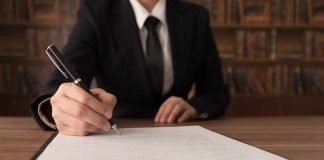 Person in suit signing a document on a clipboard