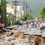 23 DEAD, Hundreds Missing – Flash Flood Destroys Region Residents walk along a heavily damaged street after a disaster