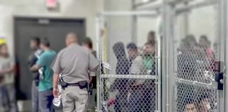 People standing inside chain-link holding area with an officer nearby