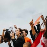 Protesters raise fists and signs as a woman speaks into a megaphone