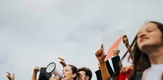 Protesters raise fists and signs as a woman speaks into a megaphone