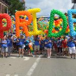 Dontrelle Inman at a Pride parade holding balloon letters spelling PRIDE