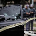 Car door with bullet holes at a taped-off crime scene
