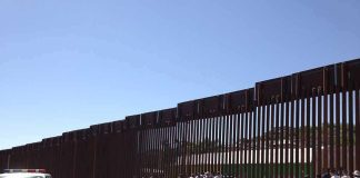 Border fence with group of people and a patrol vehicle