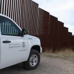 Border patrol SUV parked beside tall steel border fence