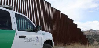 Border patrol SUV parked beside tall steel border fence