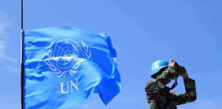 Indian Ocean War Warning Issued During U.N Address UN peacekeeper with blue helmet looks through binoculars beside UN flag