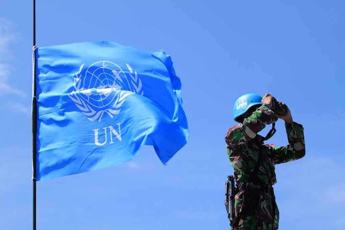 UN peacekeeper with blue helmet looks through binoculars beside UN flag