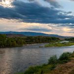 River winding through green banks under dramatic cloudy sky at sunset