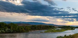 River winding through green banks under dramatic cloudy sky at sunset
