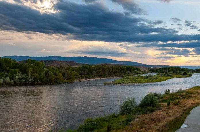 shutterstock_1499459960 River winding through green banks under dramatic cloudy sky at sunset