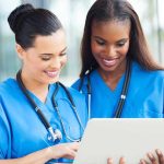 Birth-Tourism Group ARRESTED – Actively Promoting U.S Tours! Two nurses in blue scrubs looking at a tablet