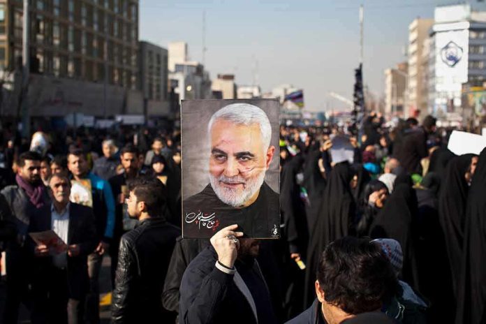 shutterstock_1609234762 Qasem Soleimani portrait held aloft in a crowded street gathering