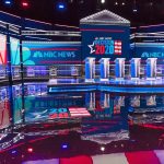 Televised debate stage with multiple podiums and bright red, white, and blue lighting
