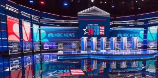 Televised debate stage with multiple podiums and bright red, white, and blue lighting