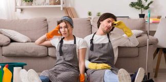 Two tired cleaners sitting on the floor by a sofa