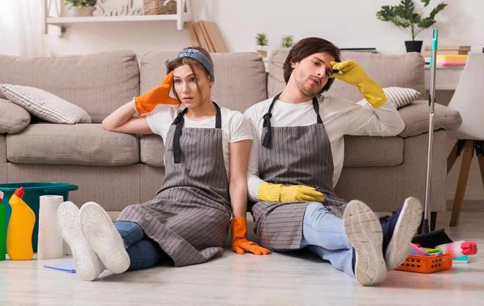 Two tired cleaners sitting on the floor by a sofa