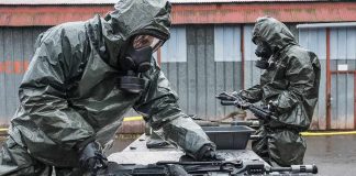 Personnel in hazmat suits decontaminating rifles on an outdoor table