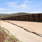 Border fence along dirt road in arid landscape