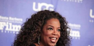 smiling woman with curly hair on a blue step-and-repeat backdrop