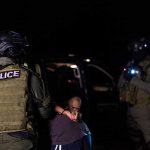 NFL Star ARRESTED – Shocking Federal Charges! Police officers detain a handcuffed person at night