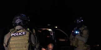 Police officers detain a handcuffed person at night