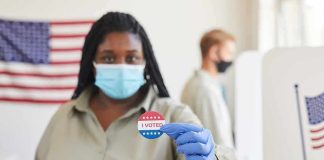 Voter wearing a mask holds an I Voted sticker at a polling place