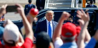 Man in suit greeted by crowd with raised hands