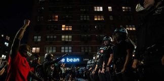 Achille Emaná kneels with raised fist facing a line of police officers at night