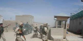 Soldiers in desert uniforms run past a checkpoint amid dust