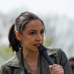 AOC Makes 2028 Decision – Official! AOC speaking into a handheld microphone outdoors