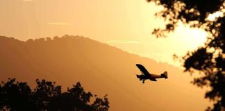 Small airplane silhouetted at sunset over tree-lined hills
