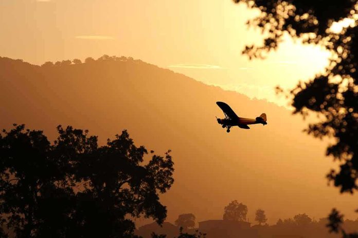 Small airplane silhouetted at sunset over tree-lined hills