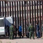 Shocking Van Dance Ignites ICE Firestorm Border agents escort a group near a tall fence and a patrol van