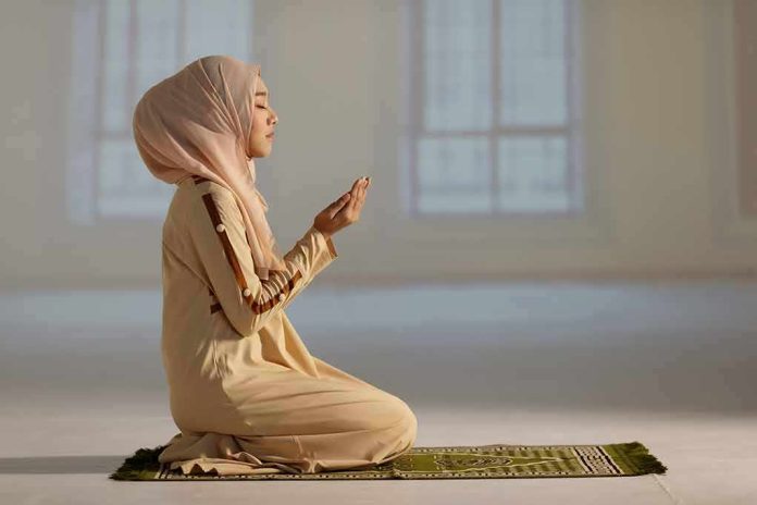 Woman in hijab praying on a mat indoors