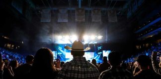 Cowboy-hatted man watches a concert in a packed arena