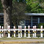 Row of white memorial crosses with flowers outside a building