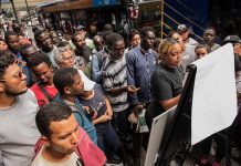Crowd gathers around a woman reading a notice board at a bus stop